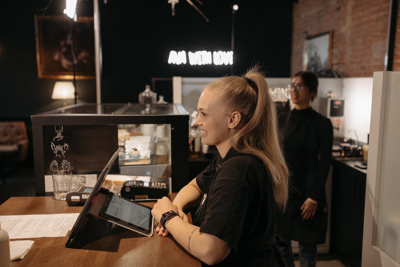 Barista smiling and serving customers at a cozy café counter with warm lighting and modern decor.